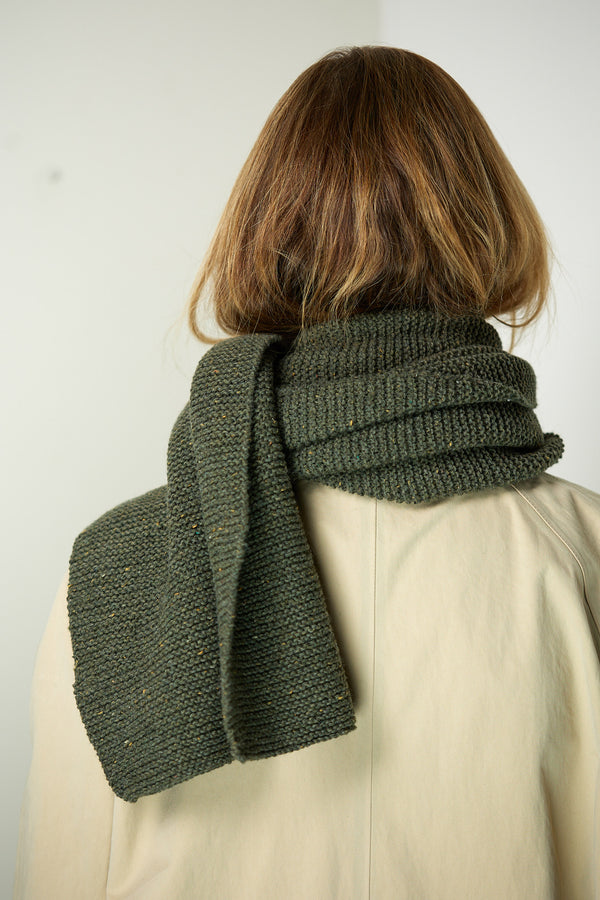 A woman seen from behind wearing a long hand-knitted scarf in Forest Green.