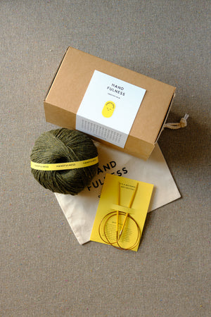 Medium Handfulness kit in Forest Green: a ball of dark green yarn, wooden needles, a cotton bag and a kraft box.