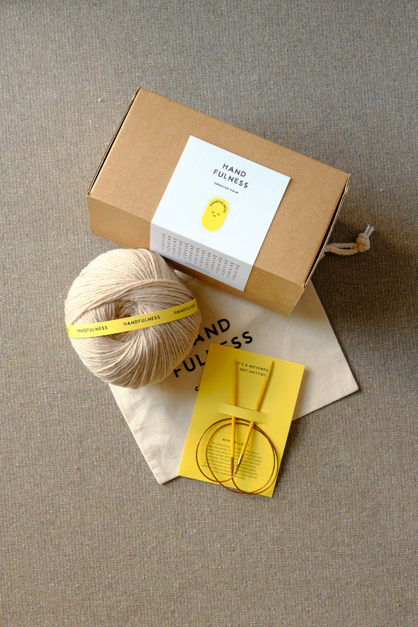 Medium Handfulness kit in Sand: a ball of beige yarn, wooden needles, a cotton bag and a kraft box.