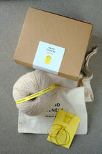 Large Handfulness kit in Sand: a ball of beige yarn, wooden needles, a cotton bag and a kraft box.