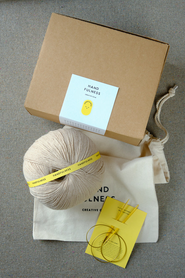 Large Handfulness kit in Sand: a ball of beige yarn, wooden needles, a cotton bag and a kraft box.