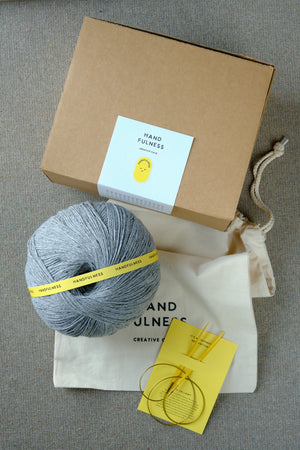 Large Handfulness kit in Cool Grey: a ball of blue-grey yarn beside the kraft box and cotton bag.